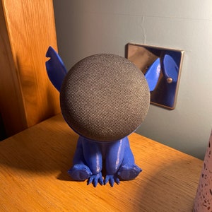 May include: Blue 3D printed Stitch character holding a round black smart speaker.