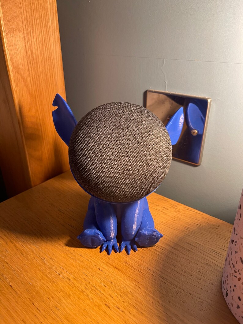 May include: Blue 3D printed Stitch character holding a round black smart speaker.