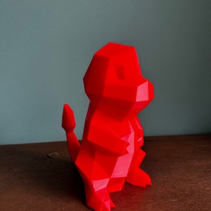 Pu&ograve; includere: Una statuetta rossa in 3D stampata in stile low-poly che rappresenta un personaggio dei cartoni animati. La statuetta ha una lunga coda e si trova su una superficie di legno.