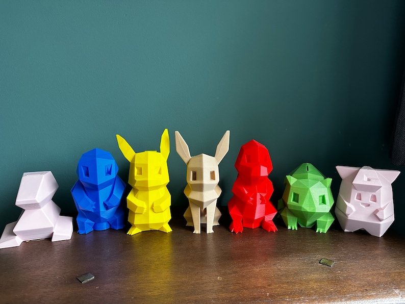 May include: A row of seven colorful, low-poly 3D printed figurines of popular cartoon characters. The figurines are arranged from left to right in the following colors: pink, blue, yellow, beige, red, green, and pink.