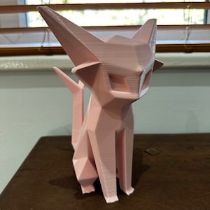May include: A pink 3D printed figurine of a cat with a geometric design. The cat is sitting with its tail curled behind it.