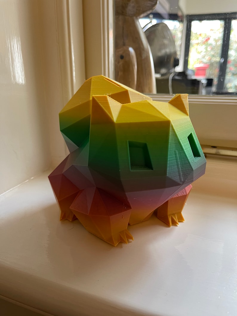 Peut inclure: Une figurine g&eacute;om&eacute;trique d'un animal de dessin anim&eacute; imprim&eacute;e en 3D avec un d&eacute;grad&eacute; de couleurs arc-en-ciel. La figurine est en plastique et pr&eacute;sente un d&eacute;grad&eacute; de couleurs jaune, vert, rouge et orange.