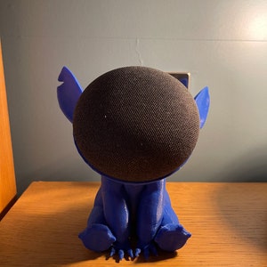 May include: A blue 3D printed figurine of Stitch from Lilo & Stitch, holding a black smart speaker.