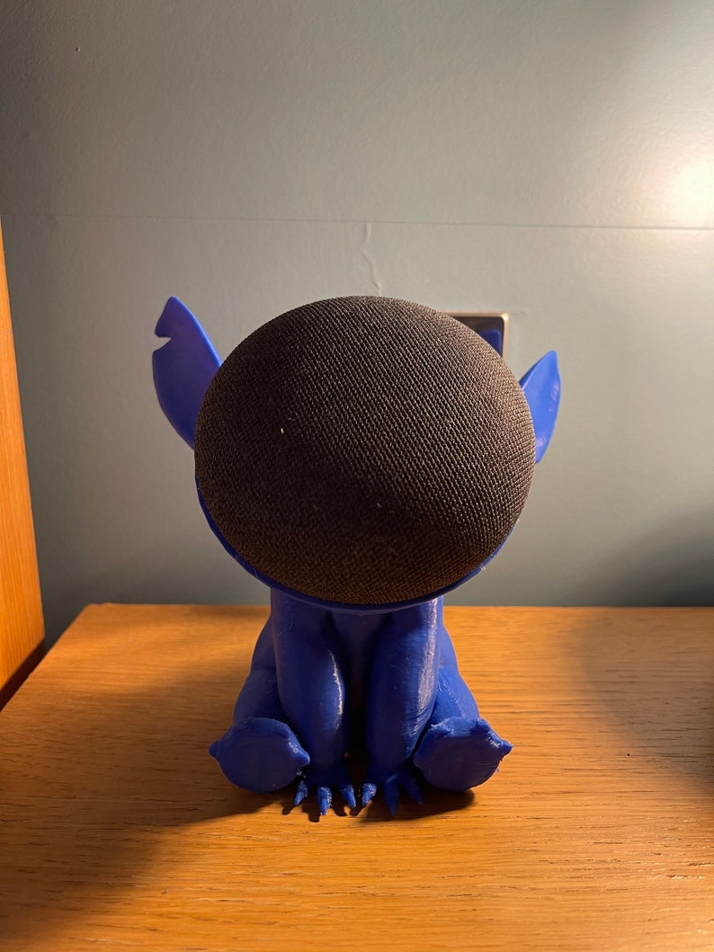 May include: A blue 3D printed figurine of Stitch from Lilo & Stitch, holding a black smart speaker.