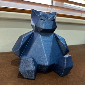 May include: A blue, geometric, 3D printed bear figurine. The bear is sitting on a wooden surface.