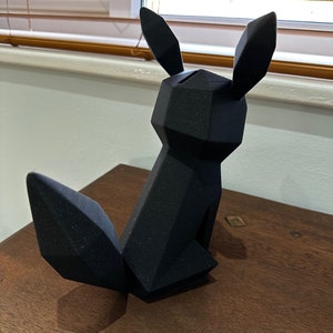 以下が含まれることがあります： 黒色の幾何学的な形をした3Dプリントされたキツネの置物。置物は表面にテクスチャがあり、木製の表面の上に置かれています。