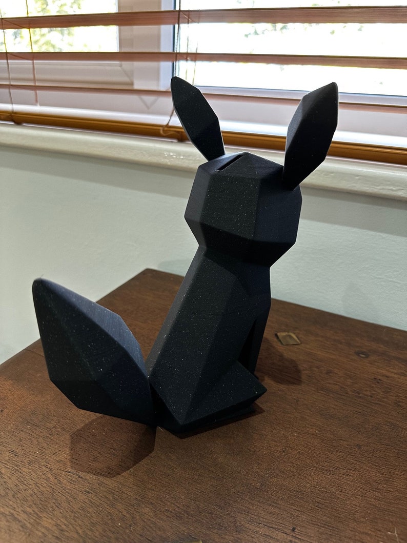 以下が含まれることがあります： 黒色の幾何学的な形をした3Dプリントされたキツネの置物。置物は表面にテクスチャがあり、木製の表面の上に置かれています。