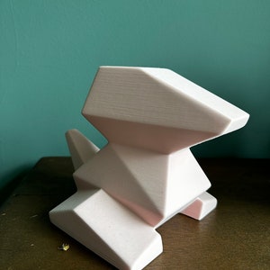 May include: A white geometric ceramic dog sculpture with a modern design. The sculpture is made of a smooth, matte material and has a simple, minimalist style.