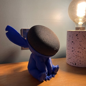 May include: A blue 3D printed character resembling Stitch from Lilo & Stitch, holding a black Google Home Mini speaker.