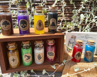 Puede incluir: Una caja de madera con dos estantes llenos de pequeñas botellas de vidrio. Cada botella tiene un tapón de corcho y una etiqueta que dice "Resistencia" con un símbolo diferente en cada una. Los símbolos incluyen una nube, una calavera, un rayo, un matraz, una estrella, una cabeza de carnero, una mano, un cerebro, una llama y un copo de nieve. La caja está sentada sobre una superficie de arpillera.