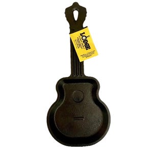 May include: A black cast iron skillet shaped like a guitar with a long neck and a rounded body. A yellow rectangular tag is attached to the neck, featuring the text LODGE CAST IRON, Seasoned Cast Iron Guitar Skillet, 4.8 x 6.25 inch, and contact details.