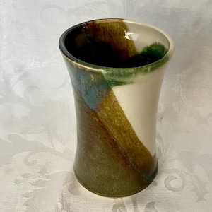 May include: A cylindrical ceramic tumbler featuring a hand-applied glaze with distinct color blocking. The exterior displays a diagonal transition between a creamy off-white section and a textured blend of earthy brown, olive green, and deep charcoal.