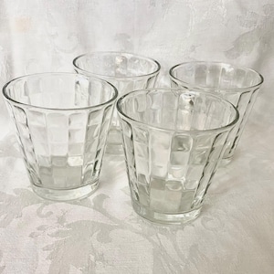 May include: A set of three clear glass tumblers, each featuring a distinct grid-like textured pattern on the exterior. The glasses have a wide, open top and a slightly tapered base, showcasing a transparent design that catches the light.