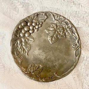 Puede incluir: Una bandeja de servir de metal plateado con un diseño de vid. La bandeja presenta un racimo de uvas y hojas en relieve.
