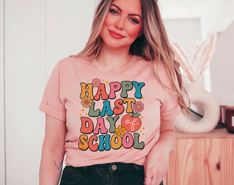 May include: A pink t-shirt with the text "Happy Last Day of School" in colorful retro letters and a red apple graphic.
