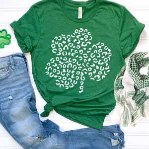May include: A green t-shirt with a white shamrock design. The shamrock is made up of white leopard print spots.