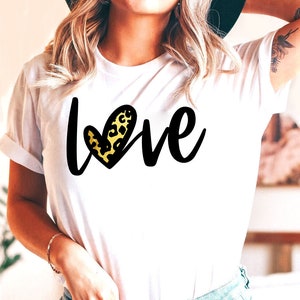 May include: White t-shirt with the word "love" written in black script with a leopard print heart in the middle of the word.