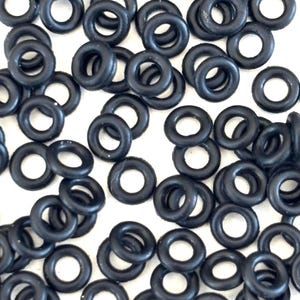 Peut inclure: Gros plan sur une collection de joints toriques noirs en caoutchouc. Les joints, de forme circulaire, présentent un trou central. Ils sont dispersés sur un fond blanc, mettant en valeur leur texture et leur forme.
