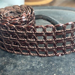 May include: A brown leather belt with a woven, grid-like pattern. The belt is made of thin strips of leather that are woven together to create a unique and stylish design.