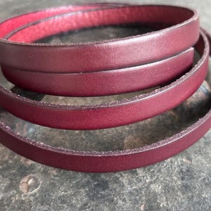 Peut inclure: Gros plan d'une ceinture en cuir bordeaux, enroulée en spirale. La ceinture a une surface lisse et polie et un intérieur rouge contrastant. Les bords du cuir sont légèrement texturés.