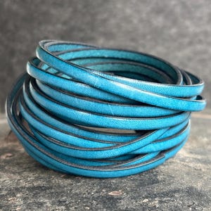 May include: A close-up of a roll of teal blue leather cord. The cord is smooth and has a slight sheen.