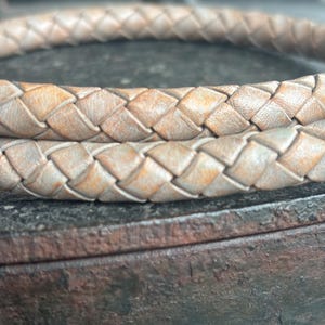 Peut inclure: Gros plan d'un cordon en cuir tressé de couleur brun clair. Le cordon est tissé en forme de losange et a un aspect légèrement vieilli.
