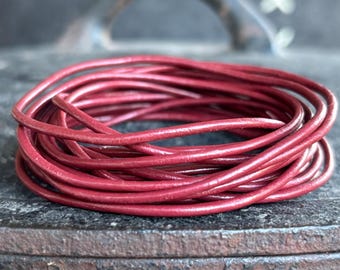 Op de afbeelding: Een spoel van bordeauxrood leren koord, strak opgerold. Het koord lijkt glad en flexibel, met een lichte glans. De achtergrond is een vage, donkere ondergrond, die contrasteert met de levendige rode tint van het leer.