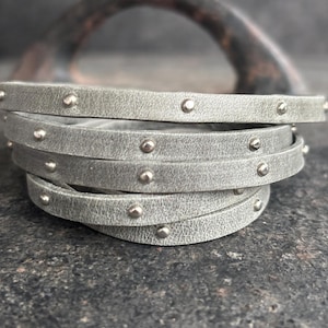 May include: A stack of five grey leather bracelets with silver studs. The bracelets are stacked on top of each other and are in focus. The background is out of focus.