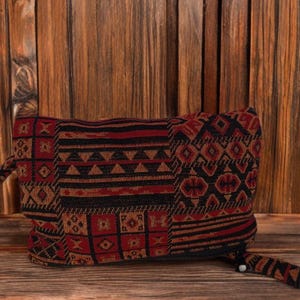 May include: A rectangular clutch bag with a geometric pattern in black, red, and brown. The bag has a zip closure and a small loop. The clutch is made of woven fabric and is suitable for carrying small items.