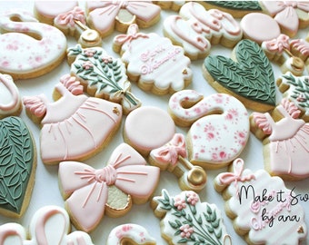 May include: A collection of decorated sugar cookies featuring a variety of designs, including swans, bows, flowers, and a dress. The cookies are decorated in shades of pink, green, and white. The text "Make it Sweet by ana" is visible on one of the cookies.