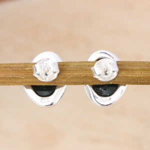 May include: A pair of silver oval-shaped earrings with black stones. The back of the earrings have the marking "925" on them.