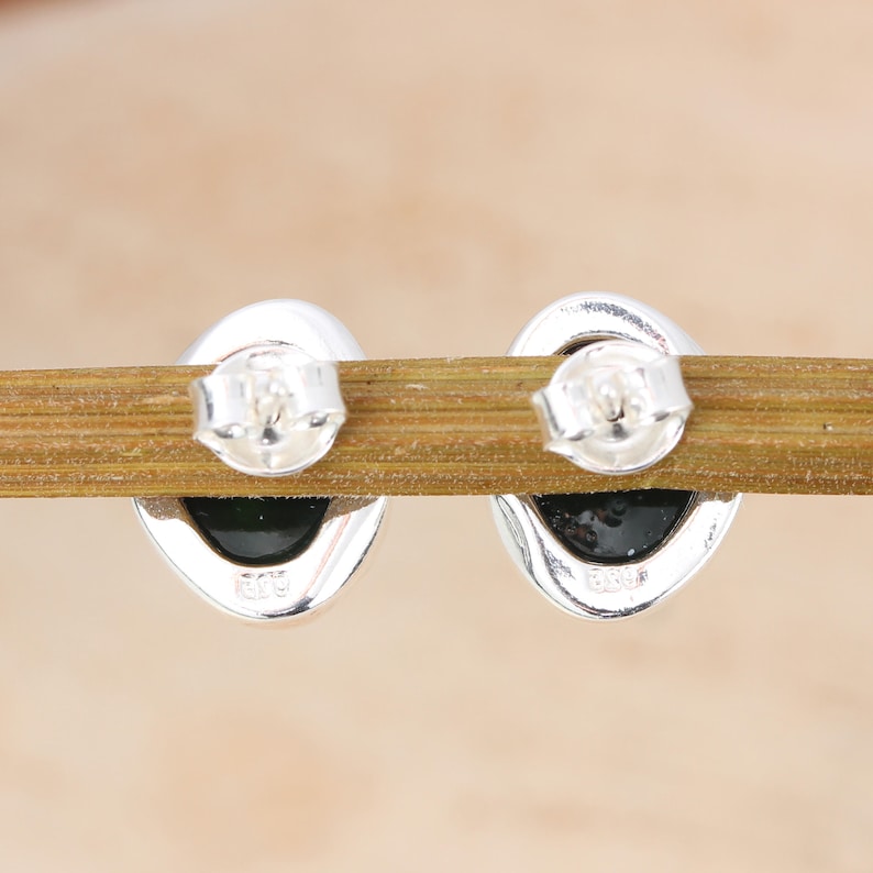 May include: A pair of silver oval-shaped earrings with black stones. The back of the earrings have the marking "925" on them.