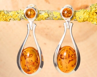 May include: A pair of silver dangle earrings with amber gemstones. The earrings feature a teardrop-shaped design with a smaller amber gemstone at the top.