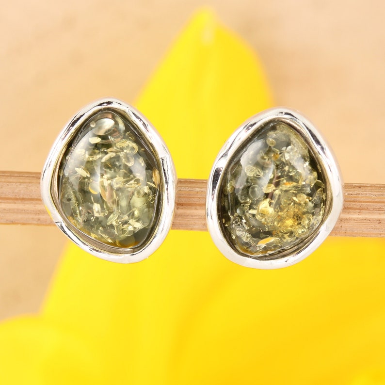 May include: A pair of silver earrings with green amber stones. The stones are irregularly shaped and have a mottled appearance.