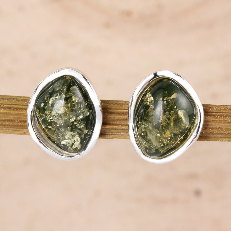 May include: A pair of silver stud earrings with green amber stones. The stones are irregularly shaped and have a speckled appearance.