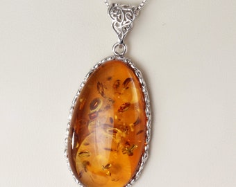 May include: A silver chain necklace with a silver filigree pendant featuring a large oval amber stone.