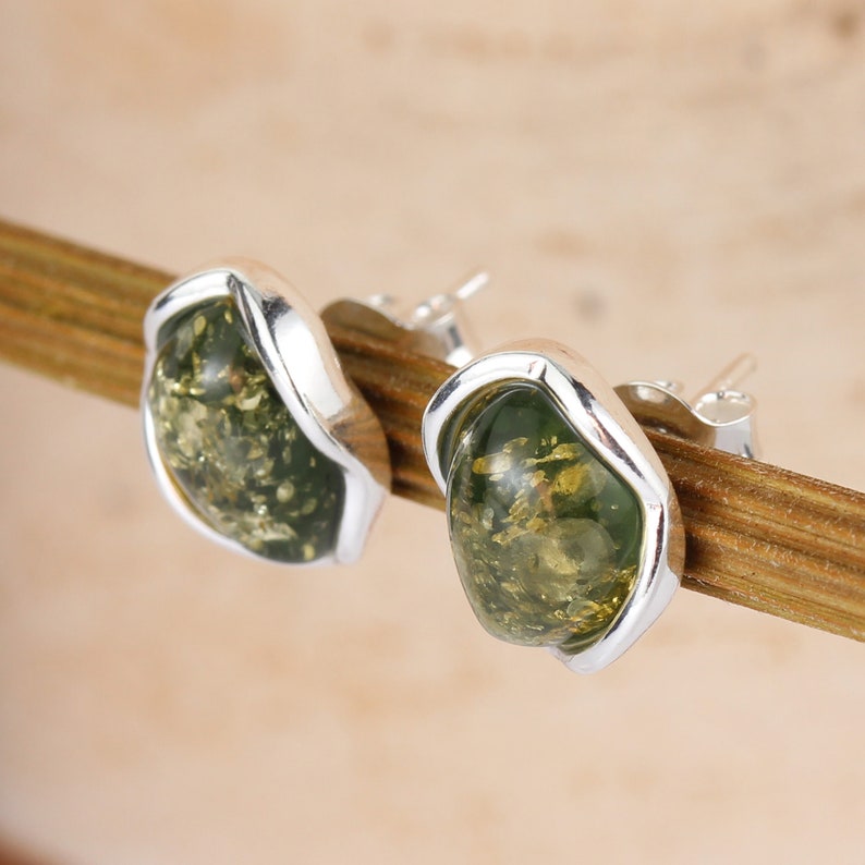 May include: A pair of silver earrings with green amber stones. The stones are set in a silver frame and have a slightly irregular shape.