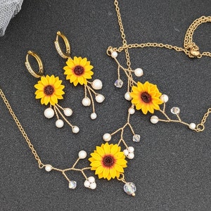 May include: A delicate gold necklace and earrings set featuring sunflower charms and pearl accents. The necklace has a vine-like design with small crystals.