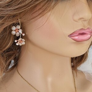 May include: Delicate floral jewelry set featuring a gold-tone necklace and earrings. The necklace and earrings are adorned with clusters of pink and white flower-shaped pendants. The earrings hang from a gold wire, and the necklace rests on the collarbone.