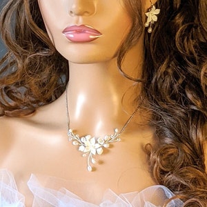 May include: A delicate white floral necklace with pearl accents and a silver chain. The necklace is worn by a model with long brown hair.