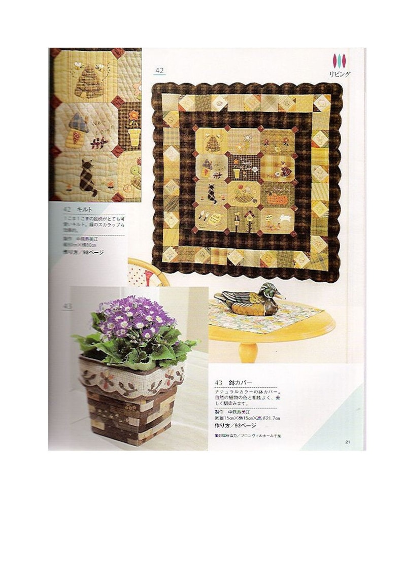May include: A close-up of a brown and beige patchwork quilt with a scalloped border. The quilt is made up of squares with different patterns and designs, including a cat, a house, and a beehive. The quilt is displayed on a table with a wooden duck figurine and a potted plant with purple flowers.