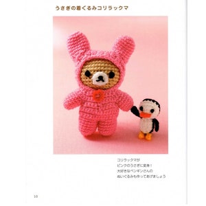 Puede incluir: Un disfraz de conejito de crochet rosa con la cabeza de un oso marrón asomando. El oso está cogido de la mano con un pequeño pingüino de crochet.