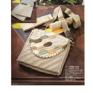 May include: A beige quilted shoulder bag with a hexagonal patchwork flap. The bag has a brown strap and is sitting on a wooden surface. The text "Six-sided flap shoulder bag" is printed in Japanese on the page.
