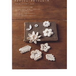 May include: A collection of delicate white crocheted flowers and leaves on a brown wooden surface. The flowers are arranged on a closed book with the word "WIFE" visible on the spine.