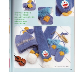 May include: A blue knitted hat, scarf, and mittens with a white pom-pom and a yellow embroidered Doraemon character. The hat has the word "Doraemon" embroidered on it in gold thread.