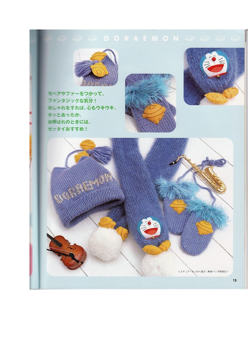 May include: A blue knitted hat, scarf, and mittens with a white pom-pom and a yellow embroidered Doraemon character. The hat has the word "Doraemon" embroidered on it in gold thread.
