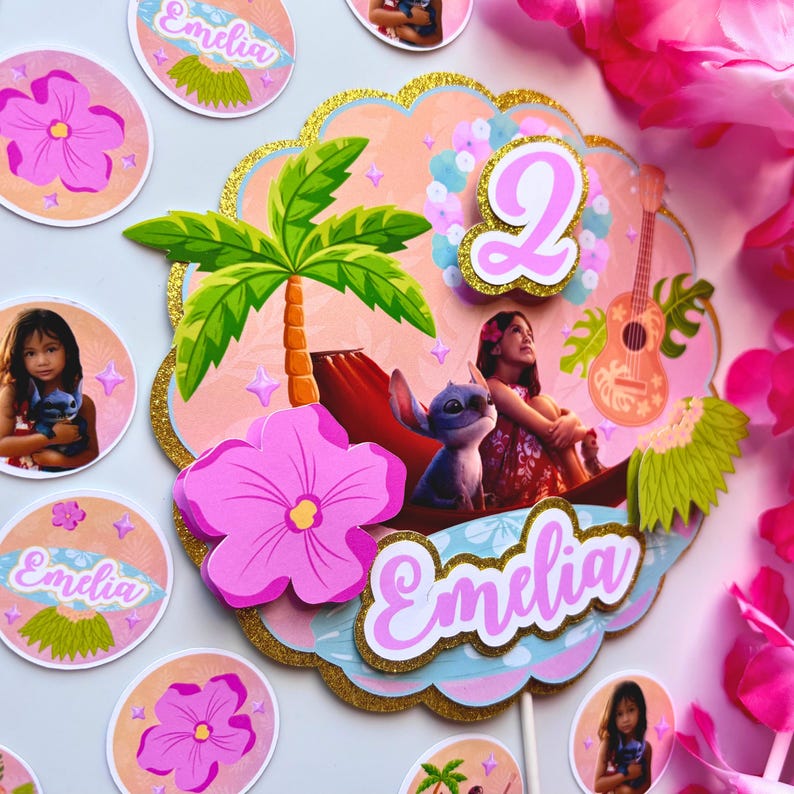 Op de afbeelding: Een tropisch thema taarttopper met een palmboom, een meisje en het personage Stitch. Het nummer 2 is prominent aanwezig, samen met de naam "Emelia" in roze script. Extra bijpassende cupcake toppers zijn ook zichtbaar, met de naam "Emelia".
