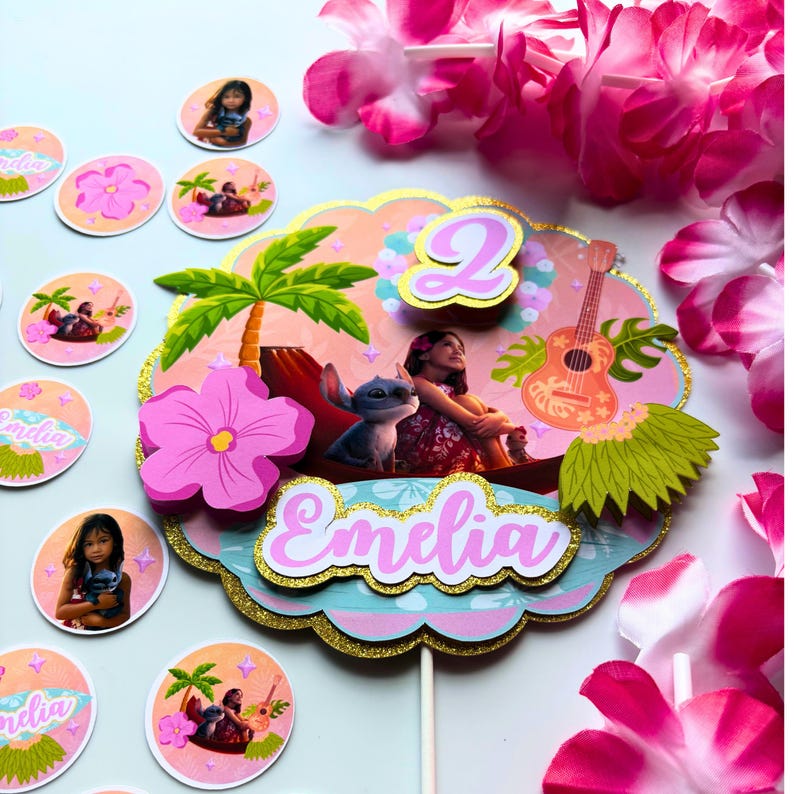 Op de afbeelding: Een kleurrijke taarttopper met de naam "Emelia" en het nummer "2". Het ontwerp heeft een tropisch thema met een meisje, een stripfiguur, een ukelele en een palmboom. Extra ronde decoraties met de naam "Emelia" en bloemmotieven zijn ook aanwezig.