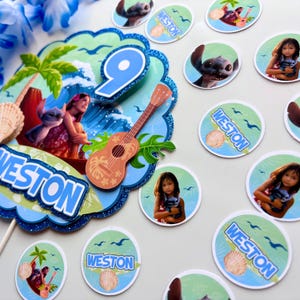 Op de afbeelding: Een feestelijke taarttopper en bijpassende cupcake toppers met een tropisch thema. De taarttopper heeft een blauwe glitterrand, een nummer 9 en een ukelele. De cupcake toppers hebben afbeeldingen van een meisje, Stitch en de naam "Weston".