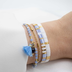 May include: A set of four bracelets featuring a mix of blue and white beads, a gold chain, and a blue tassel charm.